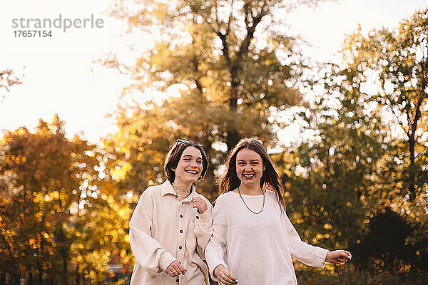 Zwei glückliche Freundinnen lächeln  während sie im Herbst im Park spazieren gehen