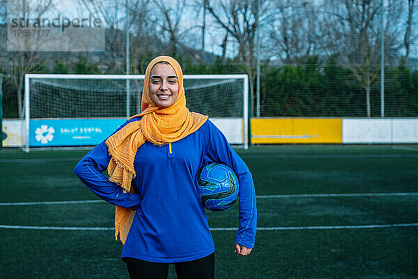 Lächelnde ethnische Frau mit Fußball auf dem Sportplatz