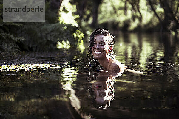 Schöne Frau lächelt beim Schwimmen im natürlichen Wasser