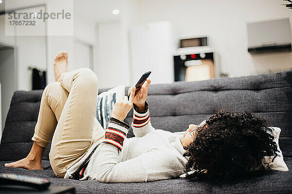 Junger Afroamerikaner blickt auf sein Handy  das auf dem Sofa seines Hauses liegt