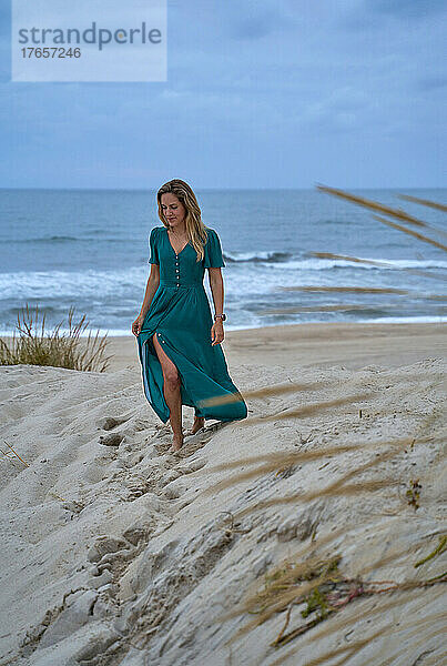 Eine elegante Frau geht an einem bewölkten Tag am Strand entlang