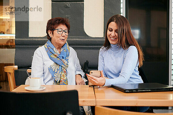 Reife Frau und junge Frau schauen in einem Café auf ein Mobiltelefon