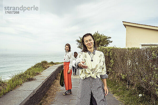 Freundlich lächelnde alternative Menschen bieten Hand für einen Spaziergang am Meer entlang