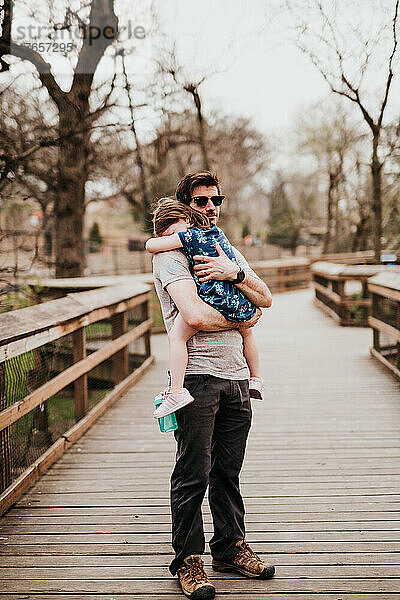 Vater hält Tochter draußen auf Holzsteg im Zoo