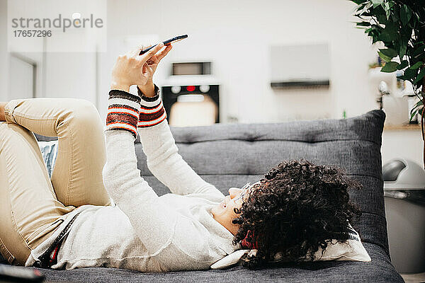 Junger Afroamerikaner blickt auf sein Handy  das auf dem Sofa seines Hauses liegt