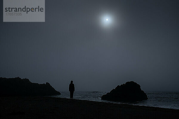 Silhouette einer Person  die an einem nebligen Tag am Strandrand steht