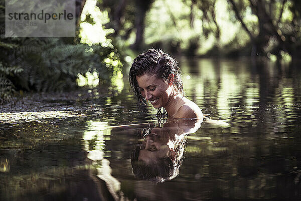 Lächelnde junge Frau im ruhigen Wasser inmitten der Natur
