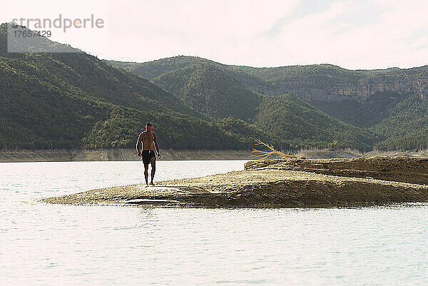 Fernsicht auf einen Mann im Badeanzug am Ufer eines Bergsees