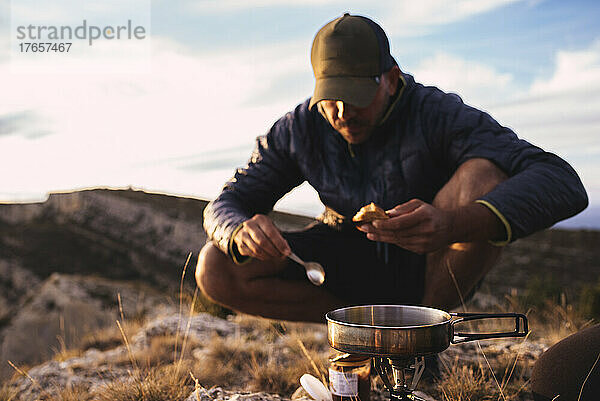 Vorderansicht eines Mannes  der während eines Campingausflugs in den Bergen kocht.