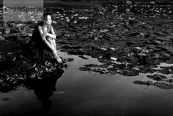 Mädchen sitzt am Ufer des Sees mit Lotusblumen