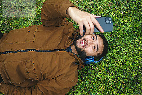Fröhlicher ethnischer Mann mit Kopfhörern  der ein Selfie mit dem Smartphone macht