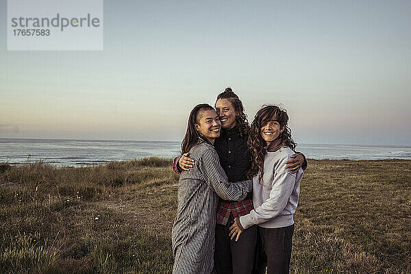 Queere Gruppe von Frauen lächelt und posiert am Meer für ein Foto