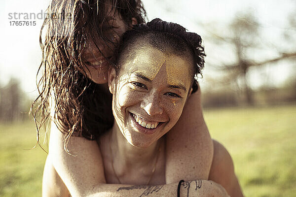 Lächelnde  glückliche queere Frauen huckepack auf der Frühlingsnachmittagswiese