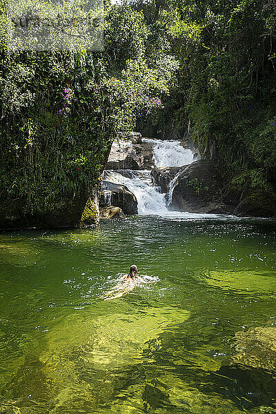 Schöne Aussicht auf eine Frau  die im grünen Pool am Regenwaldwasserfall schwimmt