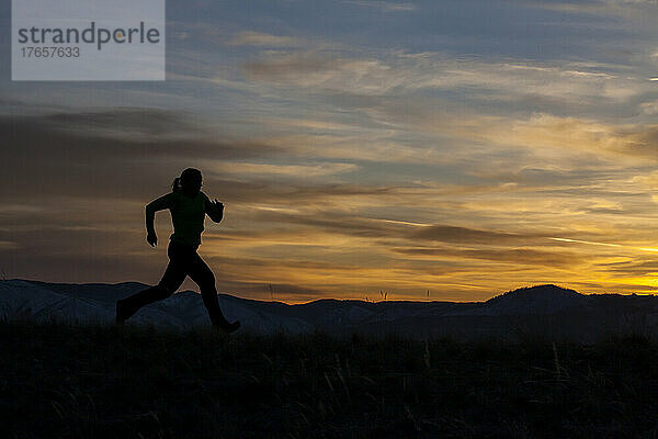 Eine Frau läuft bei Sonnenuntergang mit Bergen im Hintergrund