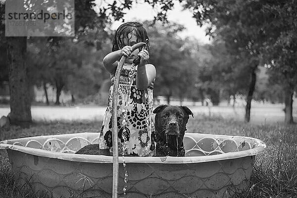 Kind und Hund spielen im Pool mit Wasserschlauch