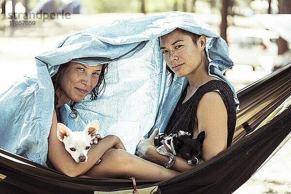 Zwei Frauen in einer Hängematte schützen sich mit Hunden vor der Sonne in Portugal