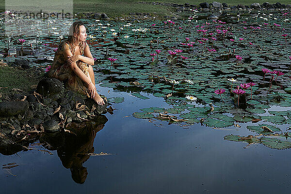 Frau sitzt mit Lotusblumen auf dem See