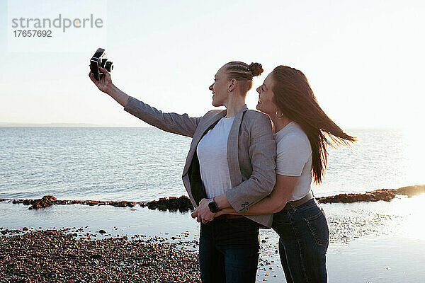 Lesbisches Paar macht Selfies am Strand bei Sonnenuntergang