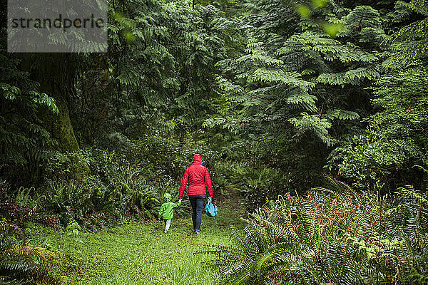 Eine Frau im Regenmantel geht mit einem kleinen Kind in den Wald