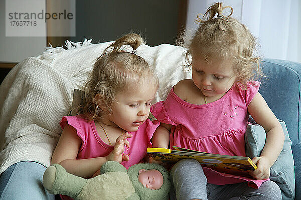 Zwillinge sitzen auf einem Stuhl und schauen sich ein Buch an