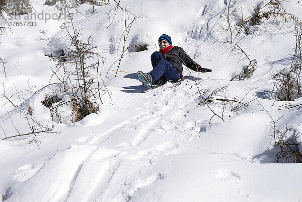 Junge rutscht vom Schneehang herunter. Genießen Sie die winterliche Rodelzeit