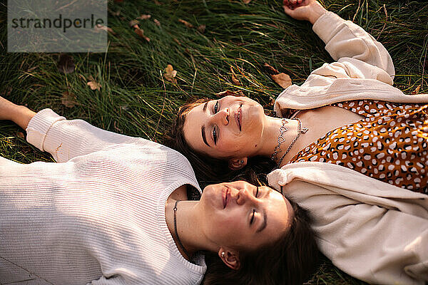 Zwei glückliche Freundinnen lächeln  während sie im Gras liegen