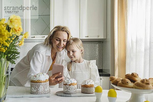 Mutter und Tochter fotografieren in der Küche mit dem Smartphone.