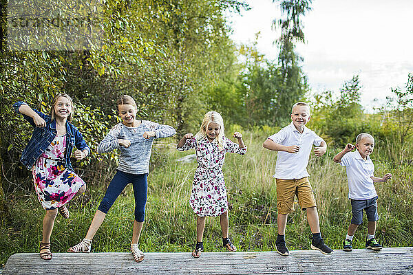 Fünf süße Kinder tanzen draußen auf einem Baumstamm