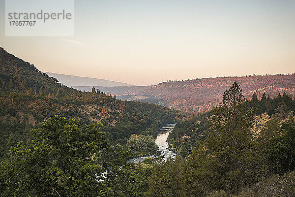 Bei Sonnenuntergang fließt ein Fluss durch bewaldete Hügel