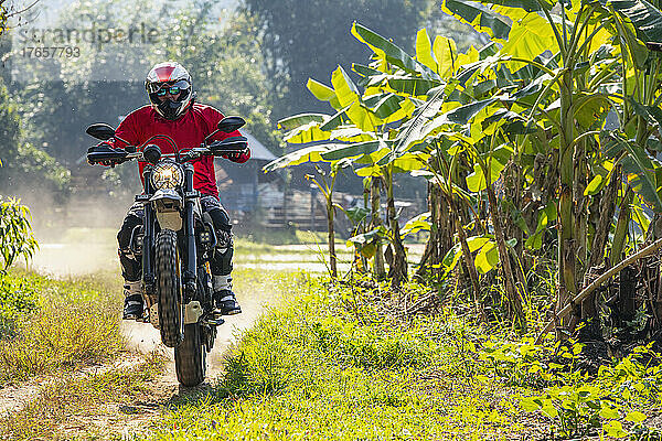 Mann fährt mit seinem Scrambler-Motorrad durch unwegsames Gelände in Thailand