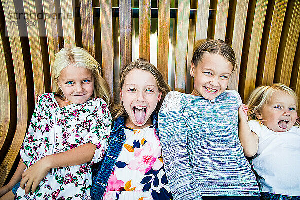 Verspieltes Porträt von vier süßen jungen Mädchen auf einer Holzbank.
