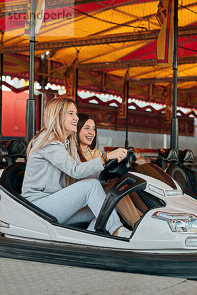 Zwei junge Frauen fahren lächelnd einen Autoscooter