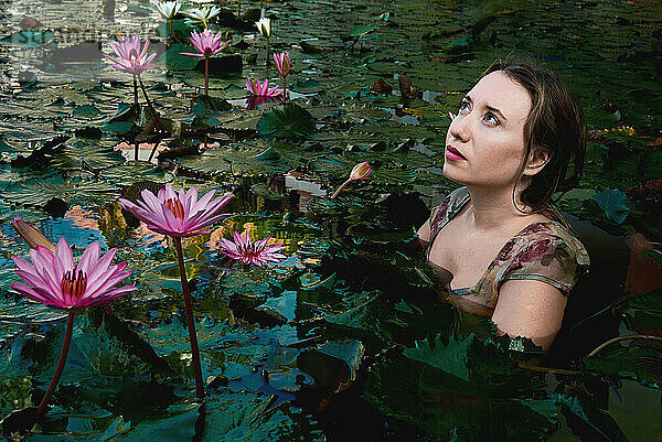 Ein Mädchen sitzt in einem See mit Lotusblumen und blickt hoffnungsvoll in den Himmel