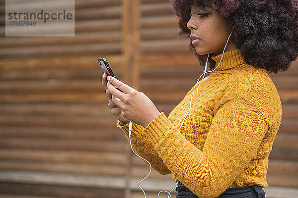 Junge Afro-Frau hört Musik auf ihrem Mobilgerät.