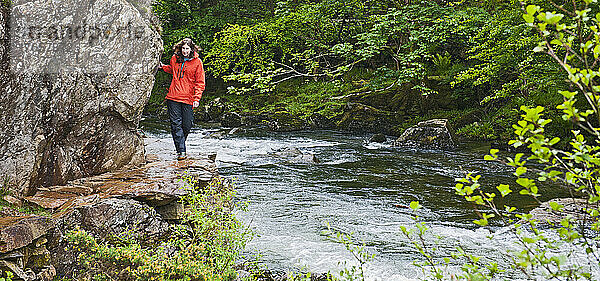Frau spaziert an einem Bach im Snowdonia-Nationalpark entlang