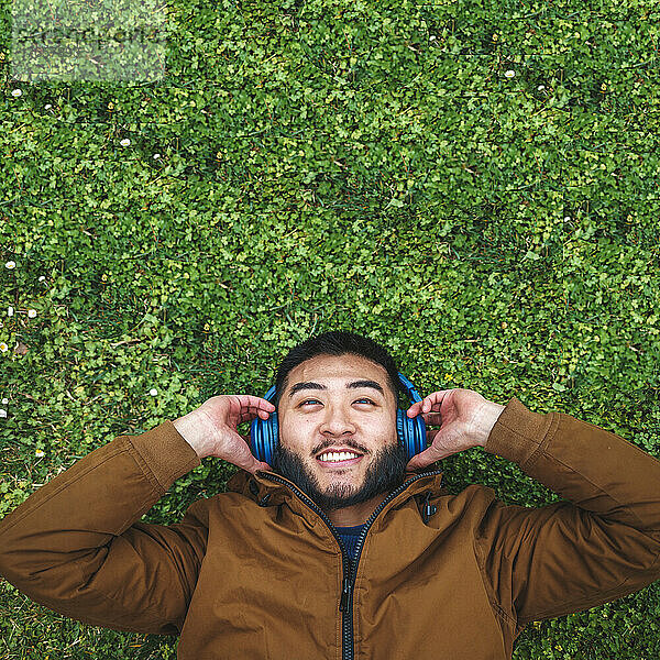 Glücklicher ethnischer Mann  der Musik mit Kopfhörern auf Gras genießt