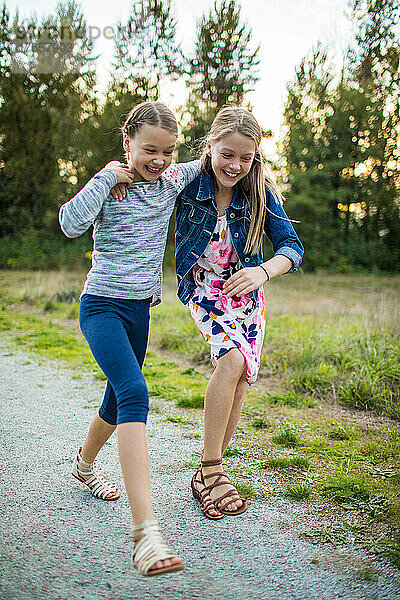 Zwei Mädchen lachen spielerisch und berühren sich unterwegs draußen im Park
