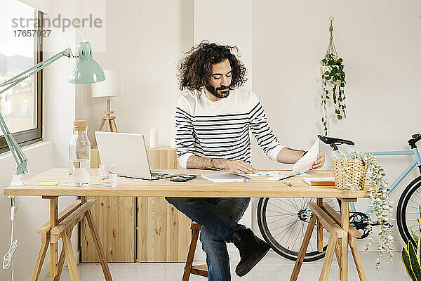 Junger Mann arbeitet im modernen Büro mit Laptop und hält Papiere in der Hand