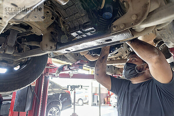 Lateinamerikanischer männlicher Mechaniker  der unter einem defekten  schmutzigen Auto arbeitet