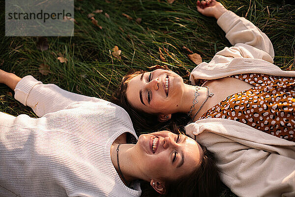 Zwei glückliche junge Frauen lächeln  während sie im Gras liegen