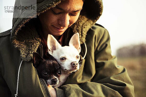 Person steckt draußen in der Nachmittagssonne zwei kleine Hunde in eine warme Jacke
