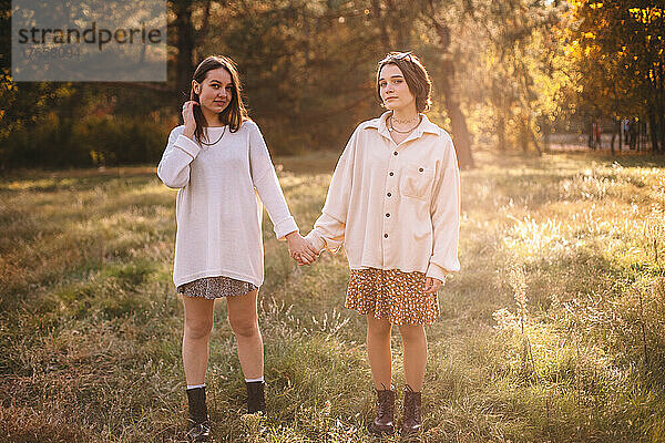 Zwei junge Frauen halten Händchen  während sie im Herbst im Park stehen