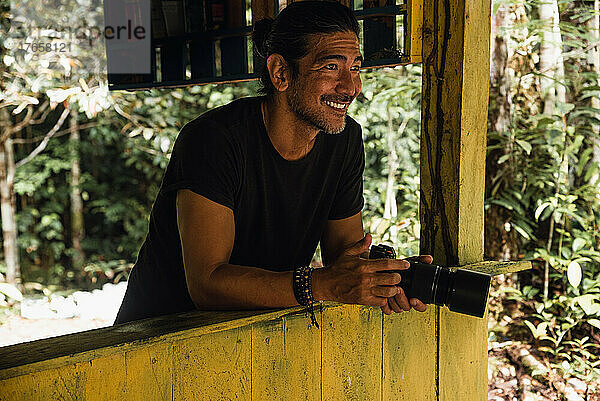 Mann lächelt mit seiner Kamera im Wald