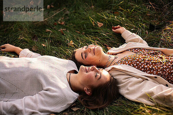 Zwei glückliche Freundinnen lächeln  während sie mit geschlossenen Augen im Gras liegen