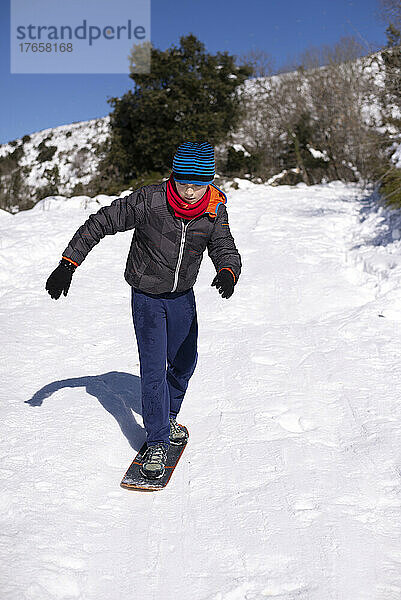 Fröhlicher Teenager reitet an einem klaren  frostigen Tag auf einem Schneehügel.