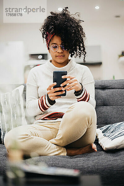 Junge Afro-Frau nutzt ihr Mobiltelefon bequem von zu Hause aus
