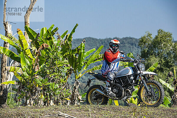 Mann mit seinem Scrambler-Motorrad auf unwegsamem Gelände in Thailand