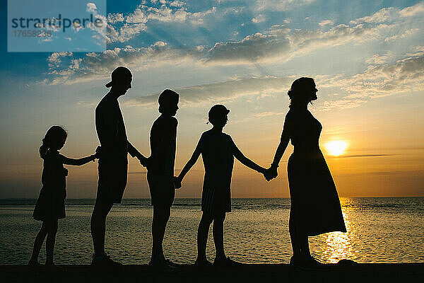Die Silhouette einer Mutter und vier Kindern vor einem Sonnenuntergang am Meer
