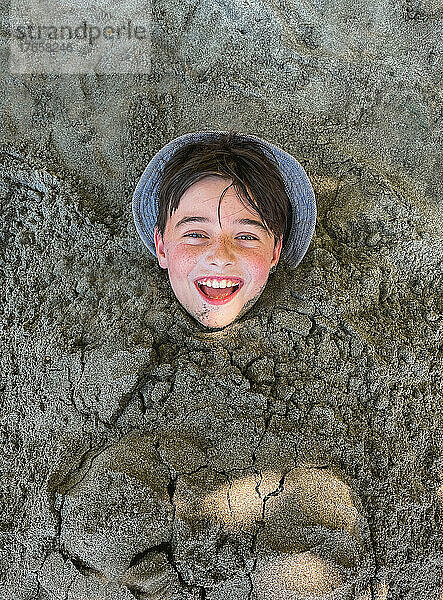 Gesicht eines glücklichen Jungen  der am Strand im Sand begraben liegt.